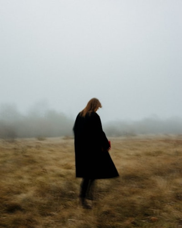 a woman in a black coat walking through a field